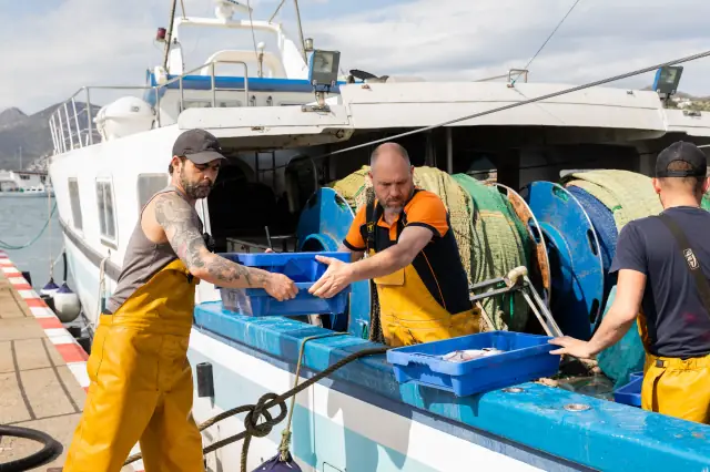 Des pêcheurs se passent des caisses de poisson à côté d'un bateau amarré au port de Roses